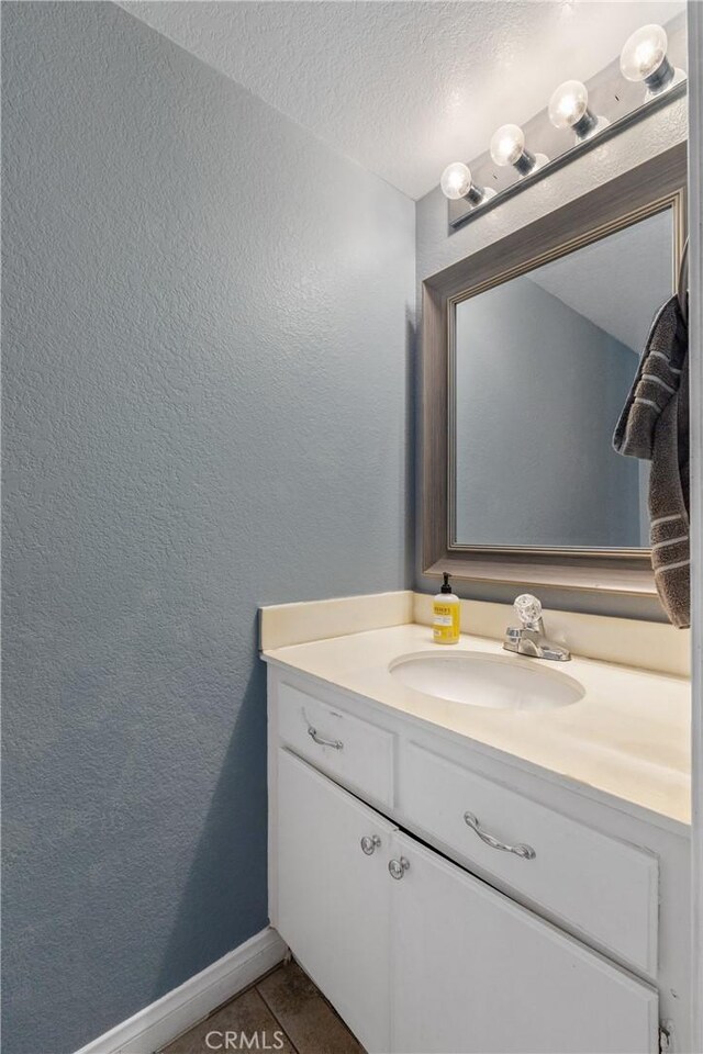 bathroom with a textured wall, tile patterned flooring, vanity, a textured ceiling, and baseboards