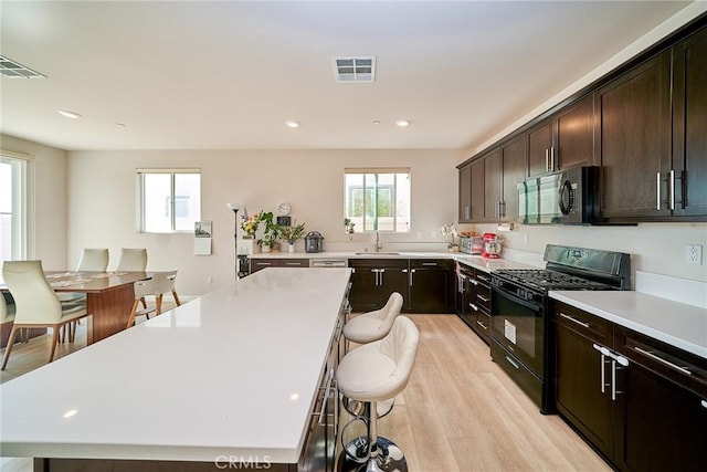 kitchen with visible vents, light countertops, a kitchen breakfast bar, black appliances, and a sink