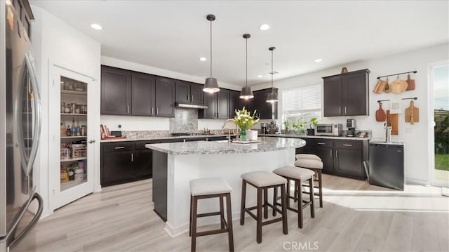 kitchen with appliances with stainless steel finishes, light wood-style flooring, a kitchen breakfast bar, an island with sink, and recessed lighting