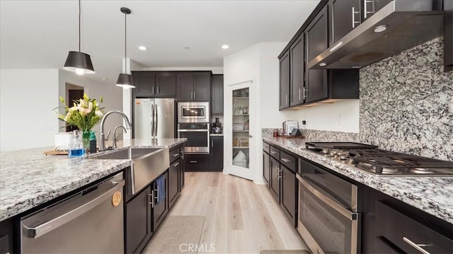 kitchen with appliances with stainless steel finishes, under cabinet range hood, a sink, light wood finished floors, and backsplash