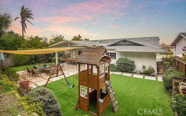 playground at dusk with a playground, fence, an outdoor hangout area, a yard, and a patio