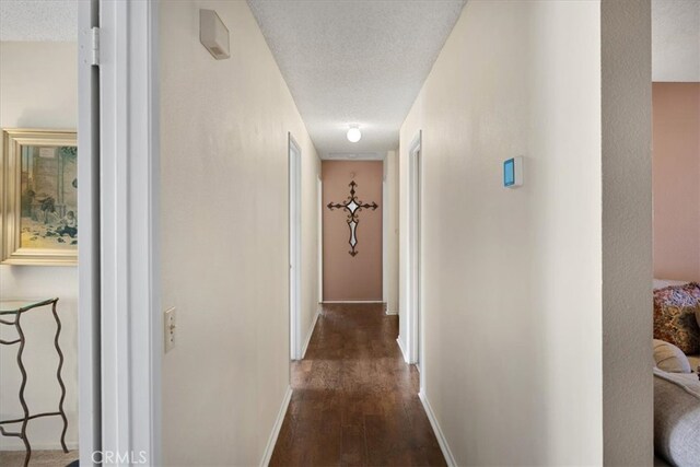 hall with dark wood-type flooring, baseboards, and a textured ceiling
