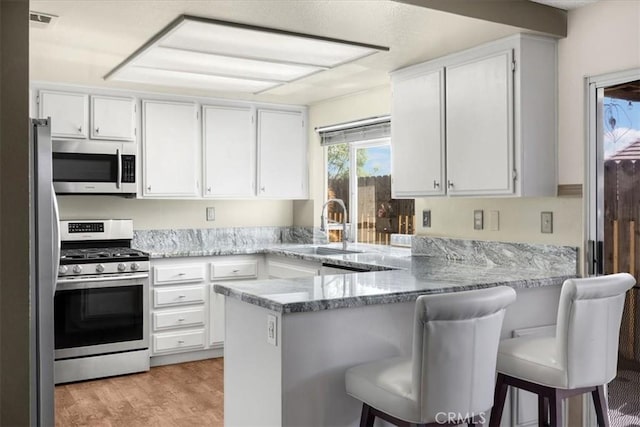 kitchen with visible vents, appliances with stainless steel finishes, a peninsula, white cabinets, and a sink