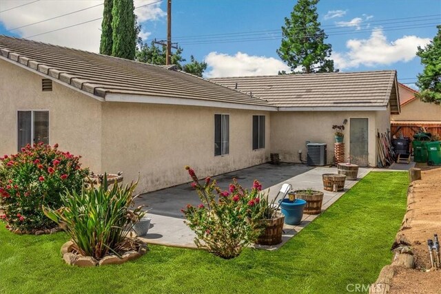 rear view of property featuring a patio area, a lawn, central AC, and stucco siding