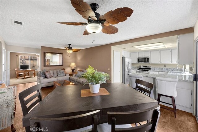 dining space featuring light wood-type flooring, visible vents, a textured ceiling, and ceiling fan