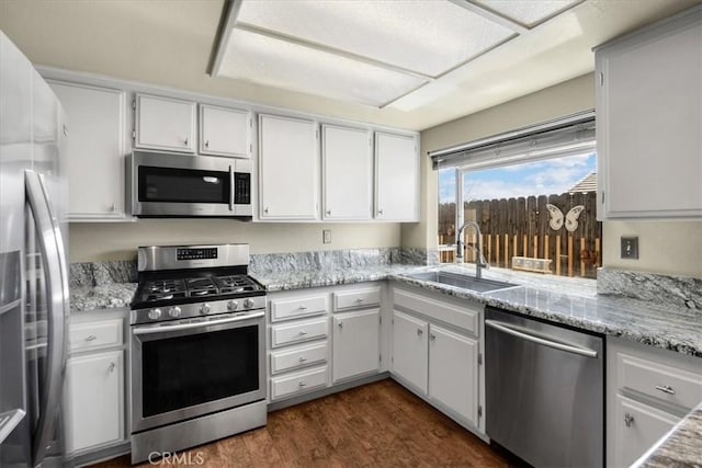 kitchen with light stone countertops, dark wood finished floors, stainless steel appliances, white cabinetry, and a sink
