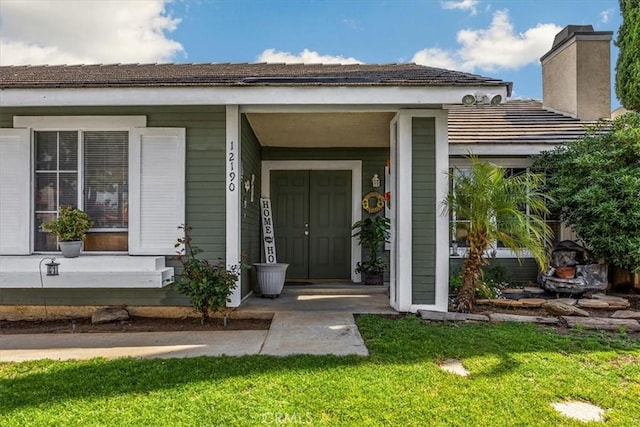 doorway to property with a porch, a tiled roof, and a lawn