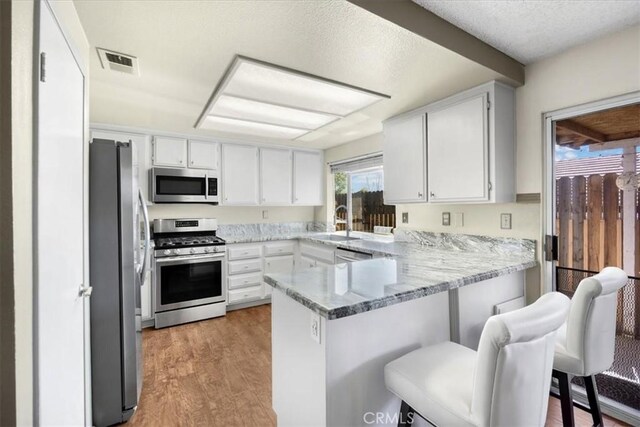 kitchen with white cabinetry, a peninsula, visible vents, and stainless steel appliances