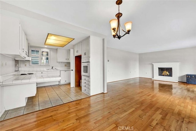 kitchen with light wood-style flooring, a sink, open floor plan, white appliances, and tile counters