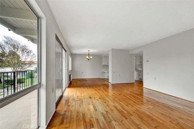 unfurnished living room with light wood-style flooring, baseboards, and an inviting chandelier