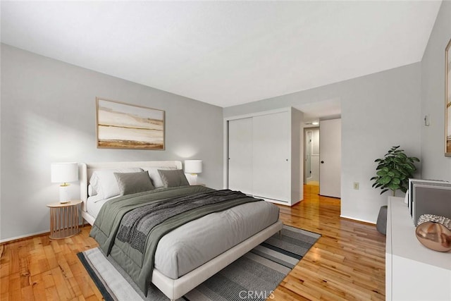 bedroom with light wood-style flooring, baseboards, and a closet
