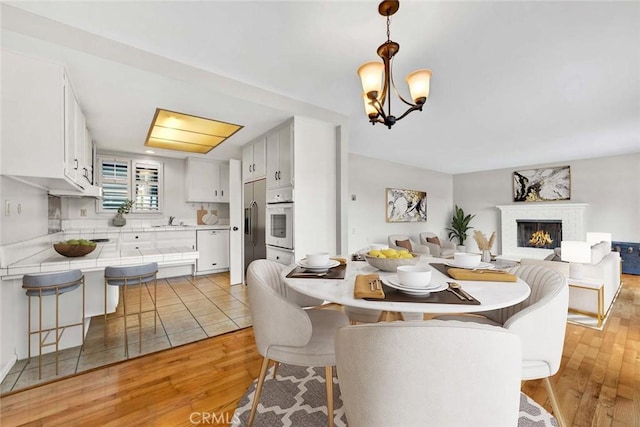 dining area with an inviting chandelier, light wood-style flooring, and a lit fireplace