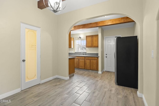 kitchen with baseboards, light wood-style flooring, arched walkways, freestanding refrigerator, and brown cabinets