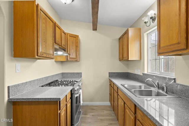 kitchen with under cabinet range hood, stainless steel gas stove, brown cabinetry, and a sink