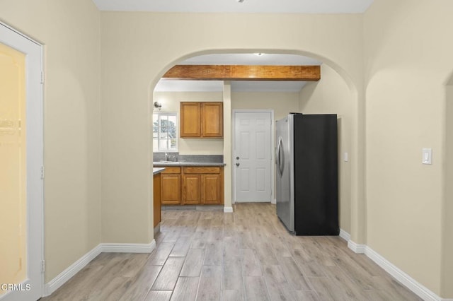 kitchen with arched walkways, brown cabinets, light wood-type flooring, and freestanding refrigerator