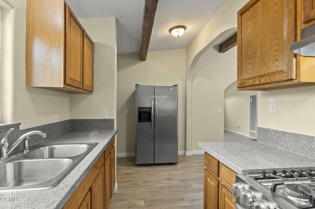 kitchen featuring brown cabinetry, beam ceiling, a sink, under cabinet range hood, and stainless steel fridge