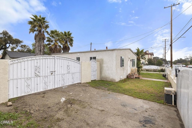 exterior space featuring stucco siding, fence, a front lawn, and a gate