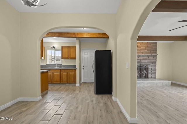 kitchen featuring light wood-type flooring, beamed ceiling, brown cabinets, and freestanding refrigerator