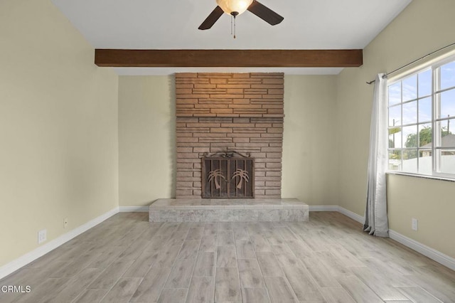 unfurnished living room featuring a stone fireplace, beam ceiling, a ceiling fan, and baseboards