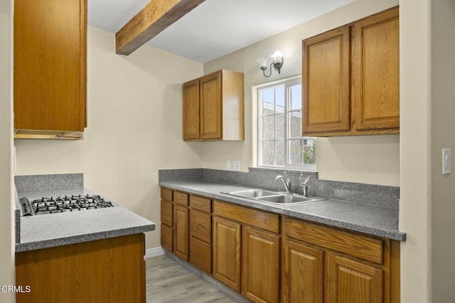 kitchen featuring stainless steel gas stovetop, brown cabinetry, beamed ceiling, and a sink