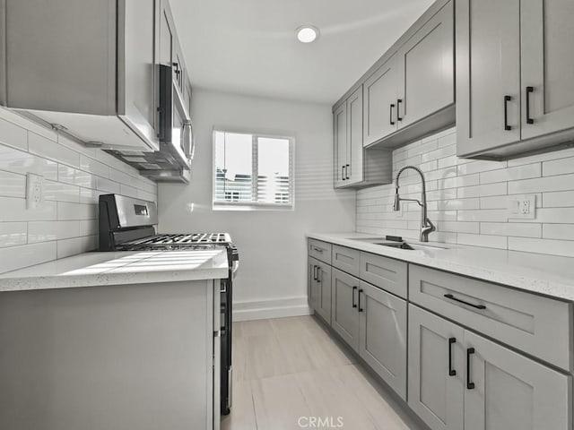 kitchen featuring a sink, decorative backsplash, appliances with stainless steel finishes, and gray cabinets
