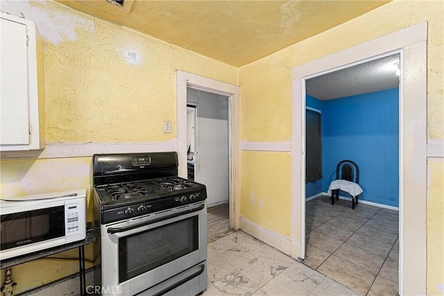 kitchen featuring white microwave, baseboards, stainless steel range with gas stovetop, white cabinets, and marble finish floor