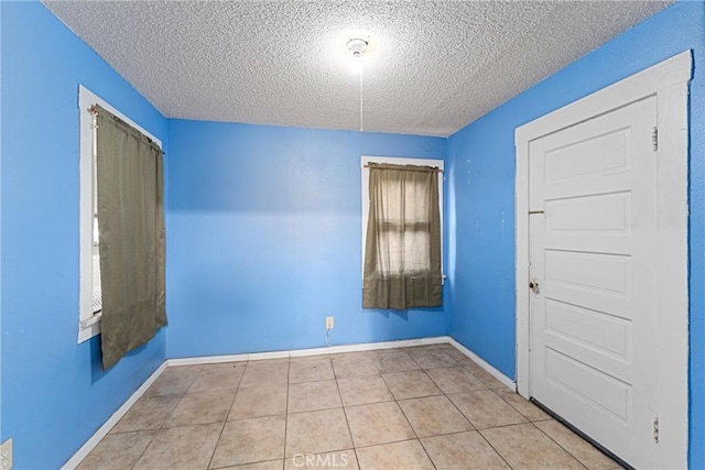 tiled empty room featuring a textured ceiling and baseboards