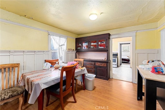 dining room featuring a wainscoted wall, washer / clothes dryer, a textured ceiling, light wood-style floors, and a decorative wall