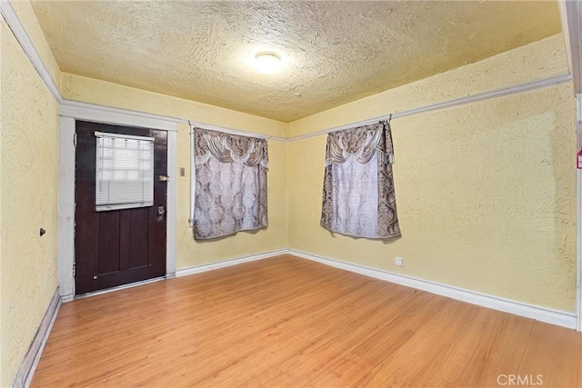 unfurnished room with a textured ceiling, a textured wall, light wood-style floors, and baseboards