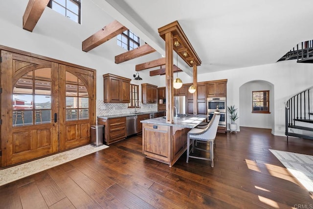 24949 Thunder Mountain Rd, Ramona, CA 92065 - kitchen featuring dark wood-style floors, arched walkways, stainless steel appliances, a kitchen bar, and tasteful backsplash