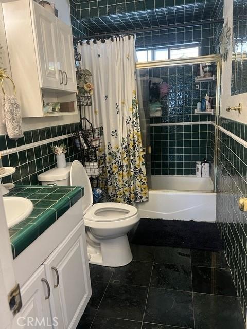 full bath with shower / tub combo, vanity, tile patterned flooring, toilet, and tile walls