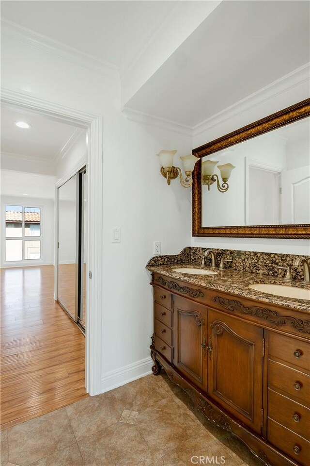 bathroom featuring double vanity, baseboards, ornamental molding, and a sink
