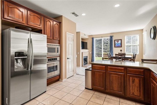 kitchen featuring light tile patterned floors, appliances with stainless steel finishes, visible vents, light countertops, and a fireplace