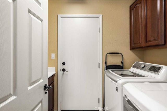clothes washing area with cabinet space, washer and clothes dryer, and a textured wall
