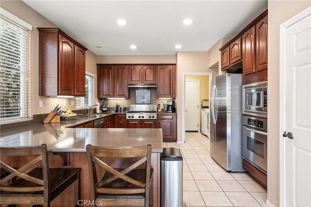 kitchen featuring a sink, independent washer and dryer, a kitchen breakfast bar, a peninsula, and appliances with stainless steel finishes