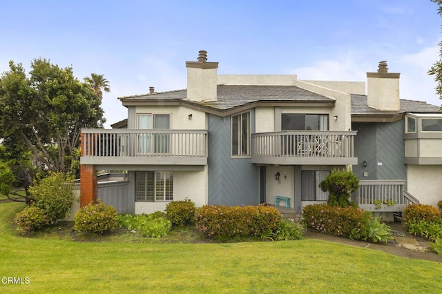 rear view of house with a balcony, a chimney, a yard, and stucco siding