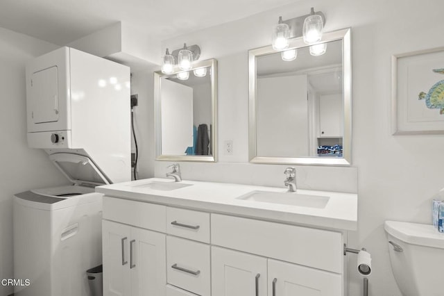 bathroom with double vanity, toilet, stacked washer and clothes dryer, and a sink