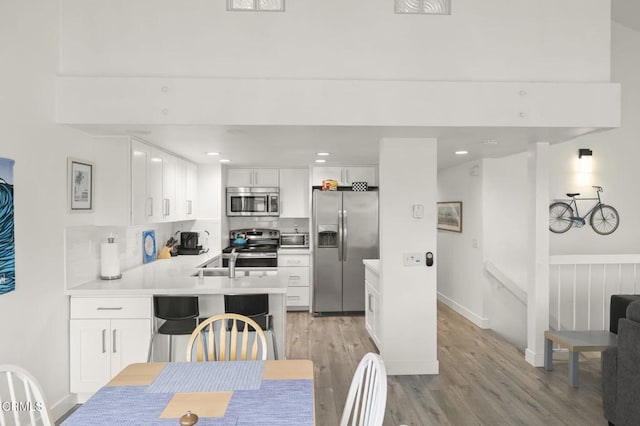 kitchen featuring a peninsula, light wood-style flooring, white cabinets, and appliances with stainless steel finishes