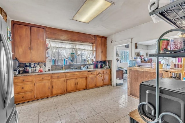 kitchen with brown cabinets, a sink, freestanding refrigerator, light countertops, and light tile patterned floors
