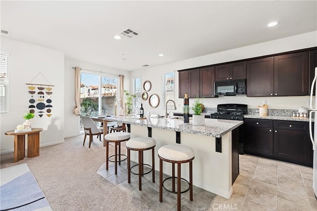 1437 Girona Dr, Pomona, CA 91766 - kitchen with black appliances, a breakfast bar area, an island with sink, light stone counters, and a sink