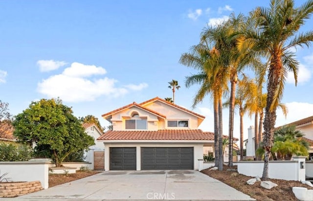 mediterranean / spanish home with stucco siding, concrete driveway, an attached garage, a tiled roof, and fence