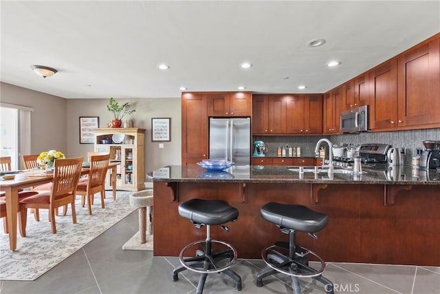 kitchen with dark stone counters, decorative backsplash, stainless steel appliances, light tile patterned floors, and a peninsula