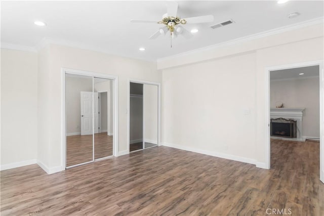 unfurnished bedroom featuring visible vents, crown molding, multiple closets, recessed lighting, and wood finished floors