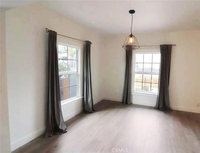 empty room featuring a wealth of natural light, baseboards, and light wood finished floors
