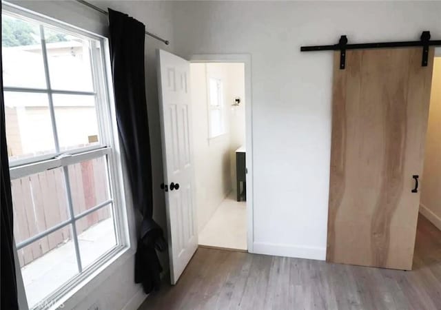 unfurnished bedroom with a barn door, light wood-style floors, and baseboards