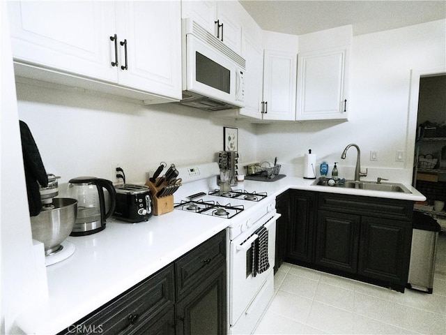 kitchen featuring a sink, white cabinetry, white appliances, light countertops, and dark cabinets