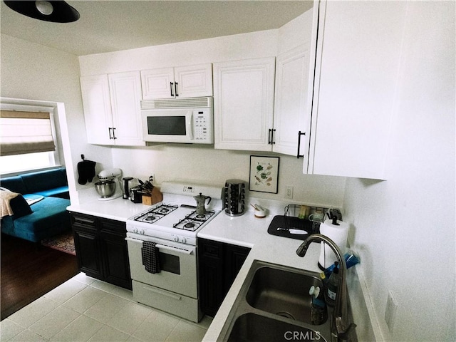 kitchen featuring light countertops, dark cabinetry, white cabinets, white appliances, and a sink