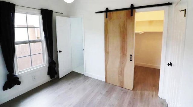 unfurnished bedroom with a barn door, light wood-style flooring, and baseboards