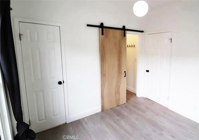unfurnished bedroom with a barn door, wood finished floors, and a closet
