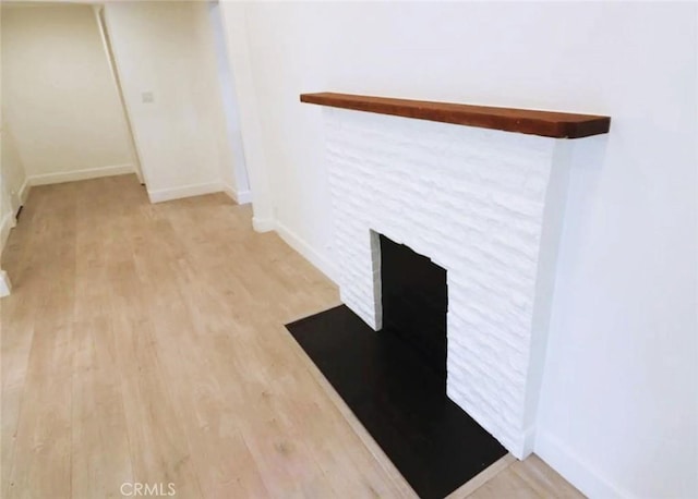 interior space with baseboards, a brick fireplace, and wood finished floors
